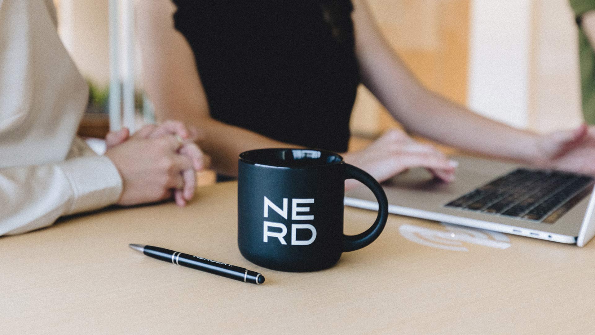 NERD mug and pen with two Nerds working on a laptop in office in the background