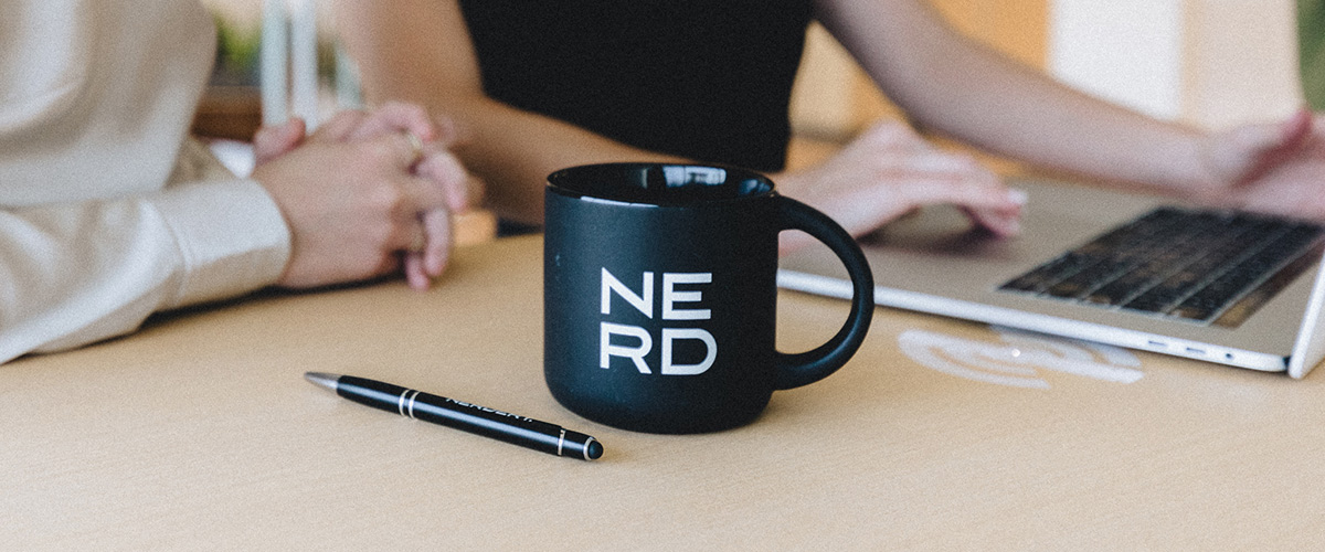 NERD mug and pen with two Nerds working on a laptop in office in the background